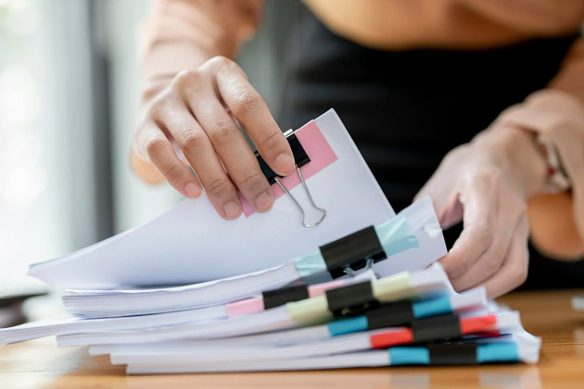 ręce osoby przeglądajacej pliki papieru, spięte dużymi spinaczami