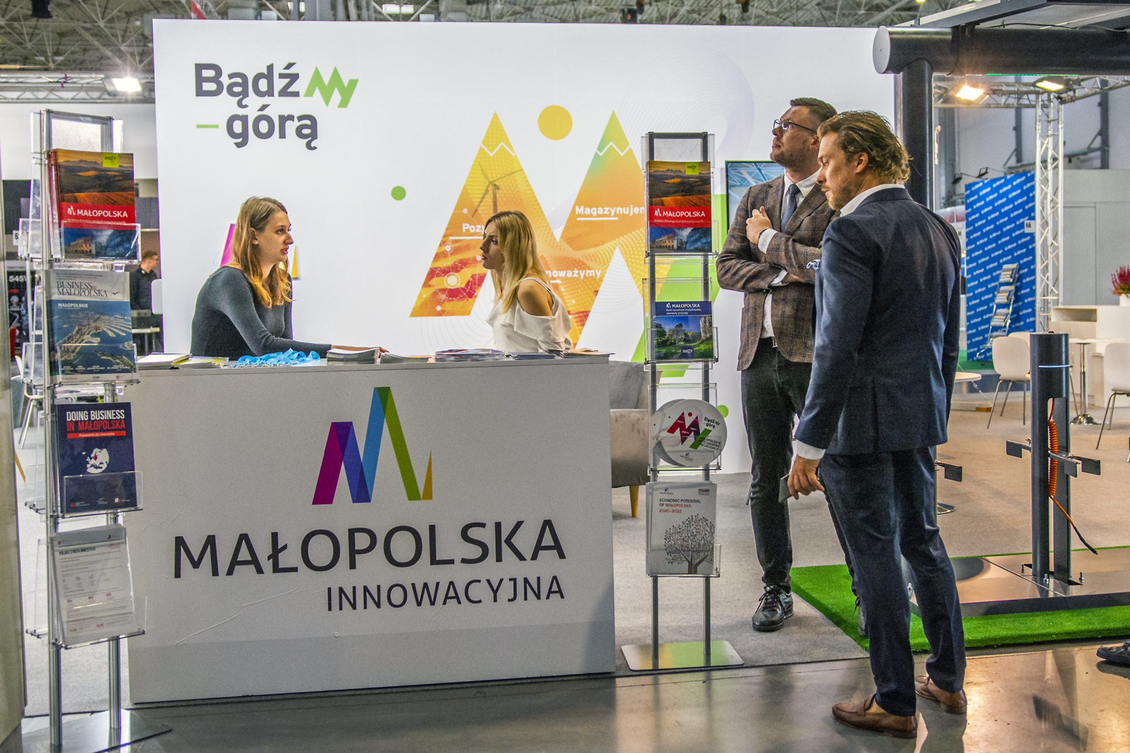 stoisko Małopolski na targach greenPOWER; za ladą dwie hostessy, obo dwóch mężczyzn; na ladzie logo Małopolski innowacyjnej